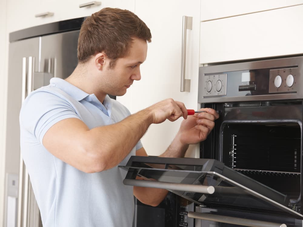 An engineer removing the door panel of a built-in oven with a screwdriver.