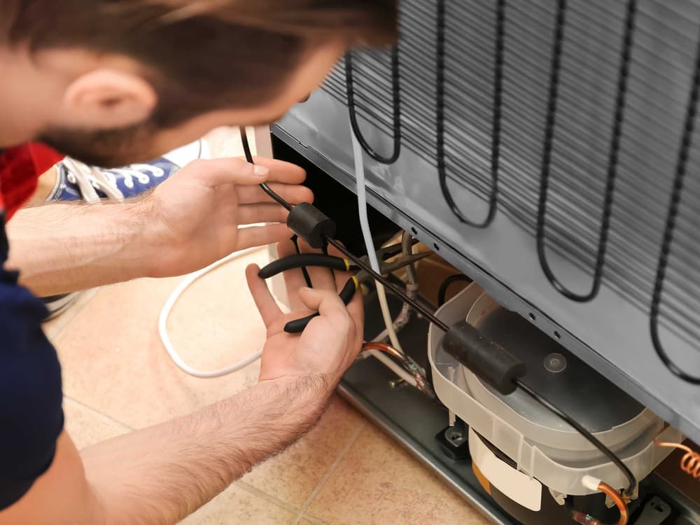 An engineer working on the condenser coils at the back of a fridge freezer.