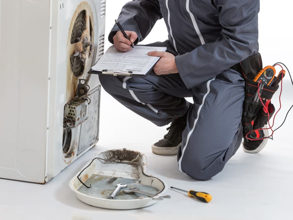 An engineer noting readings on a clipboard beside the opened back of a tumble dryer.