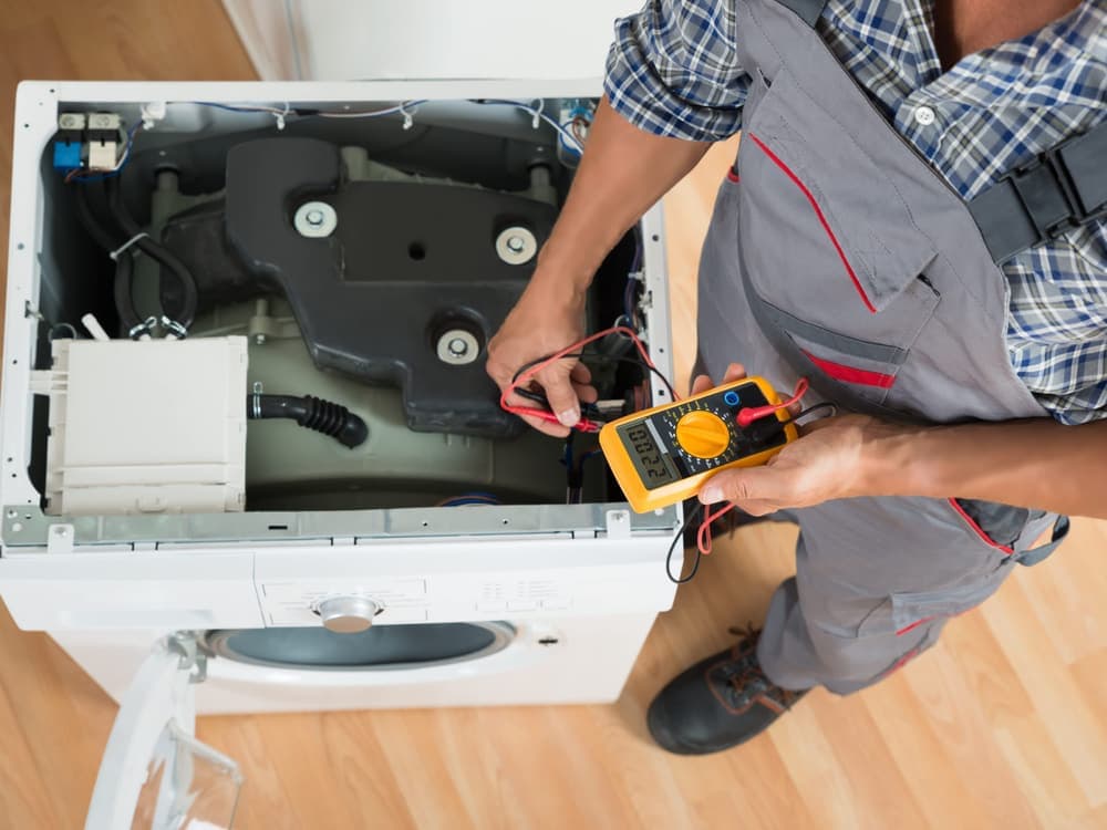 An engineer testing the wiring inside an opened washing machine with a multimeter.