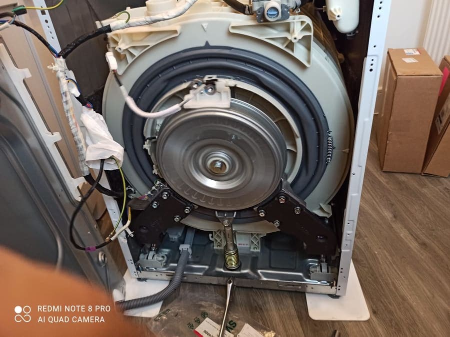 The back of a washing machine with the casing removed, exposing the drum, motor and belt.